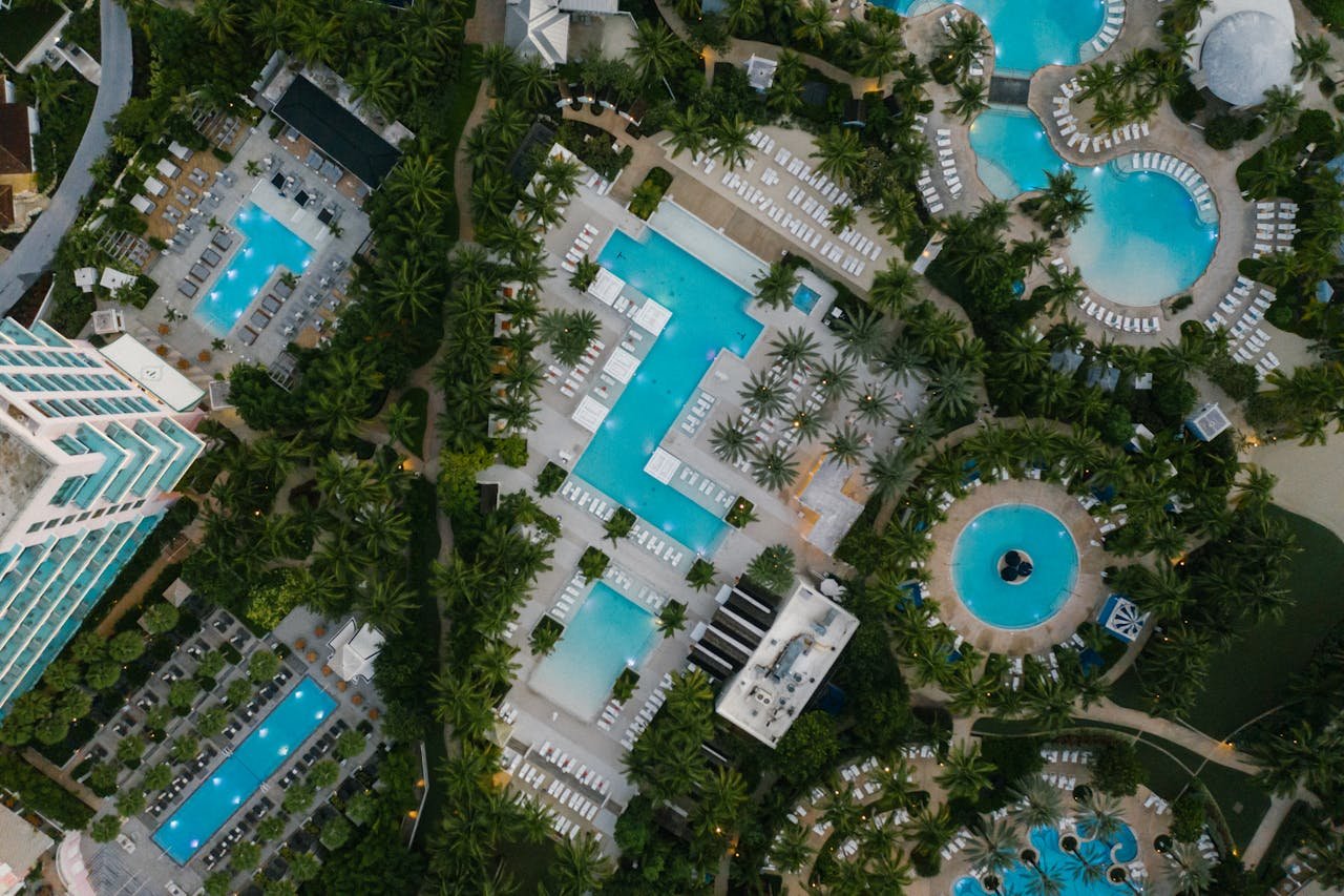 Aerial view of a luxury resort featuring swimming pools, palm trees, and elegant architecture at a tropical destination.